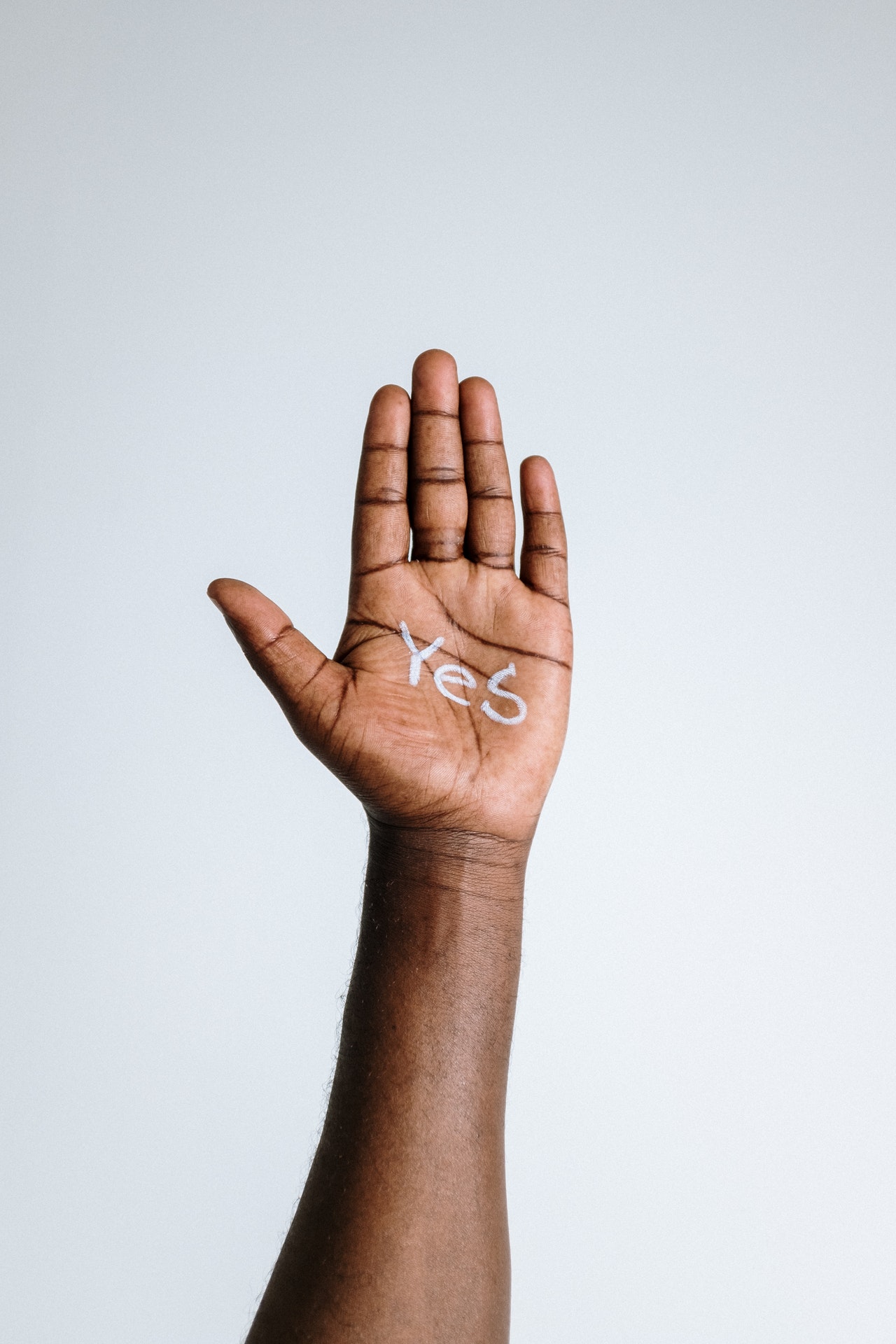 Eine dunkle Hand vor einem hellgrauen Hintergrund, in deren Handinnenfläche das Wort 'Yes' steht